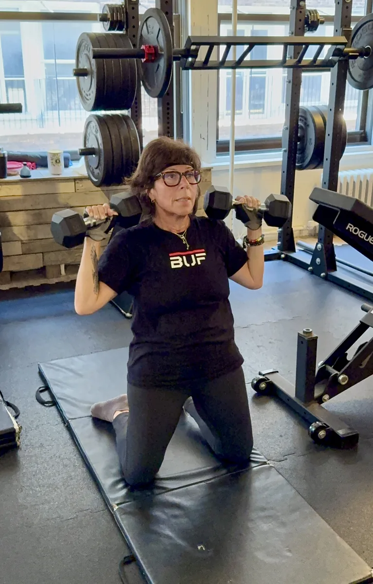 Strength training for women over 50 — older woman pressing dumbbells during a session at the BUF Over 50 studio in Midtown Manhattan